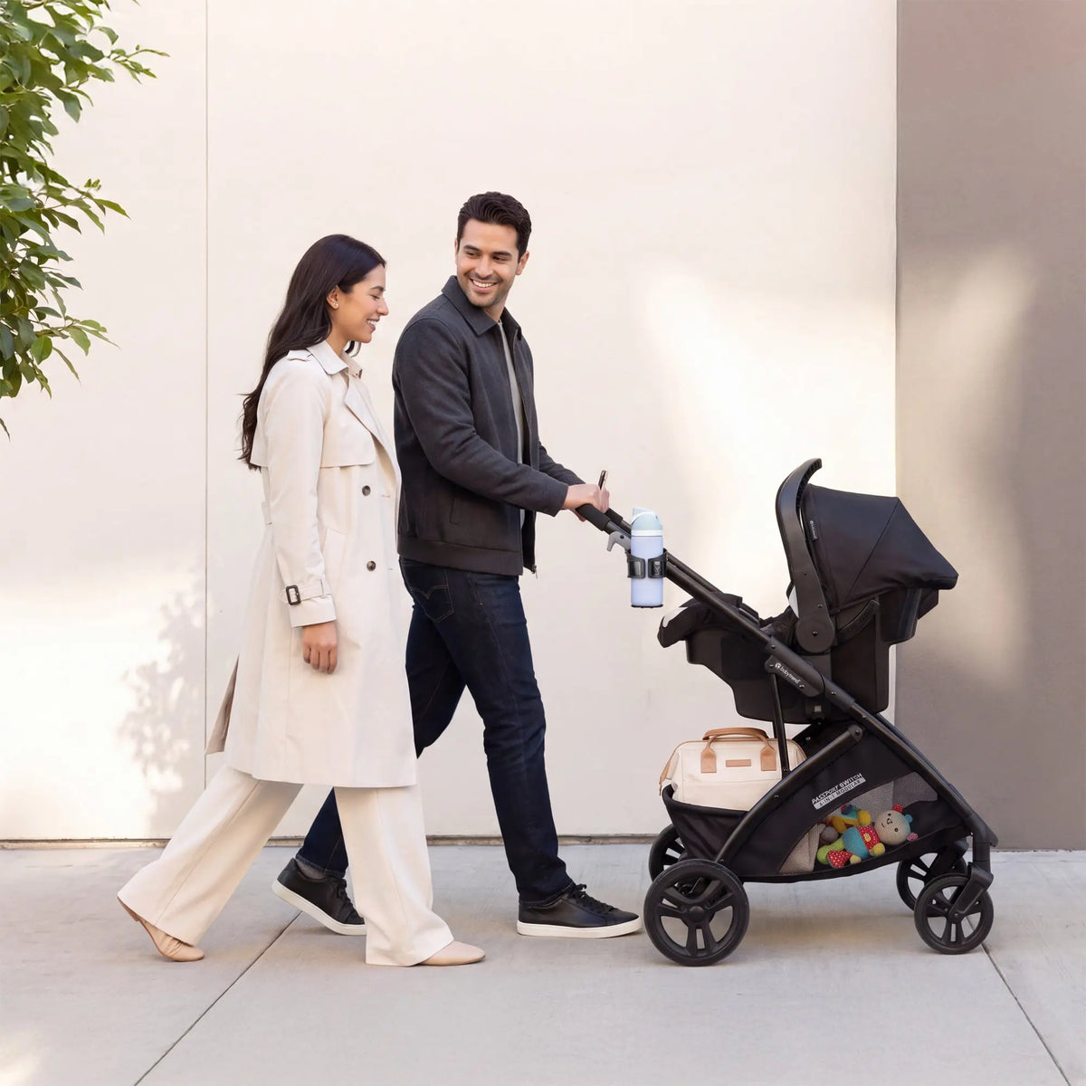 Parents walking on the sidewalk while pushing their child in the Baby Trend Passport Switch 6-in-1 Modular Stroller with the car seat attached