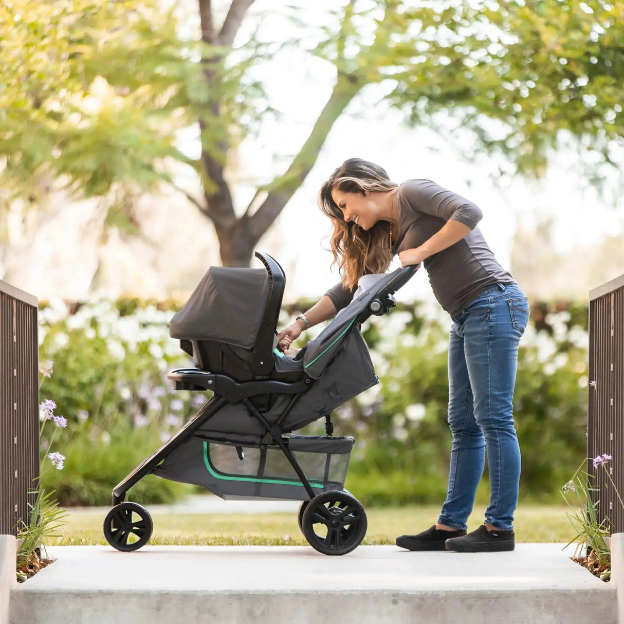 Mom is checking on her baby in the car seat on the stroller of the Baby Trend EZ Ride Stroller Travel System with EZ-Lift 35 Infant Car Seat