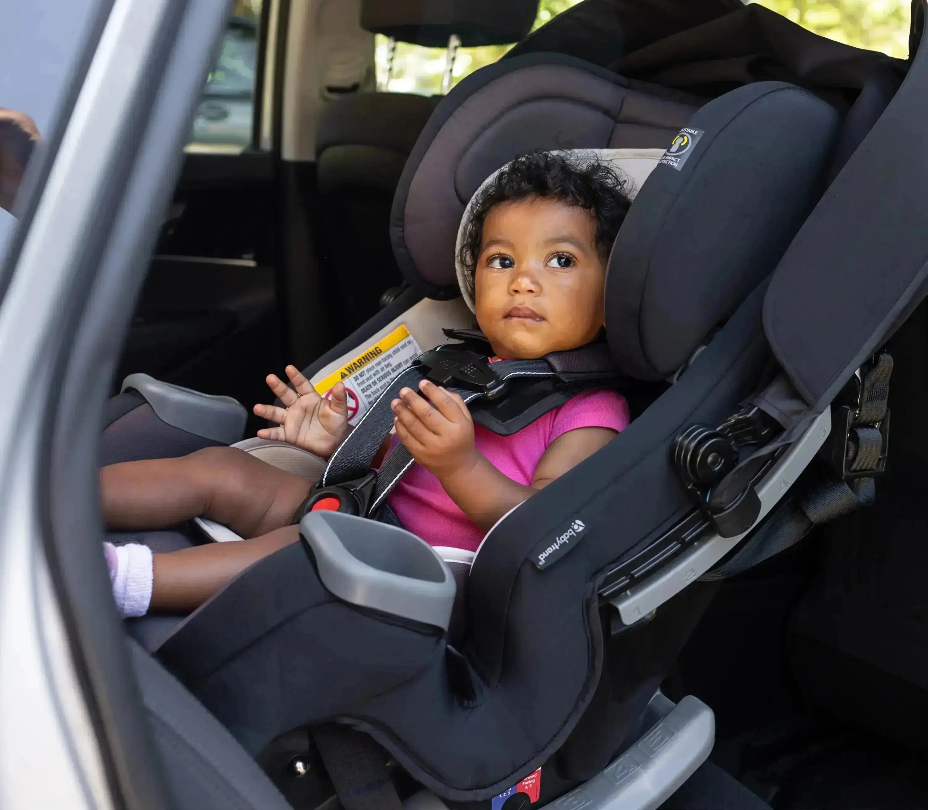 Toddler buckled into a black Baby Trend Cover Me 4-in-1 Convertible Car Seat in the back seat of a car