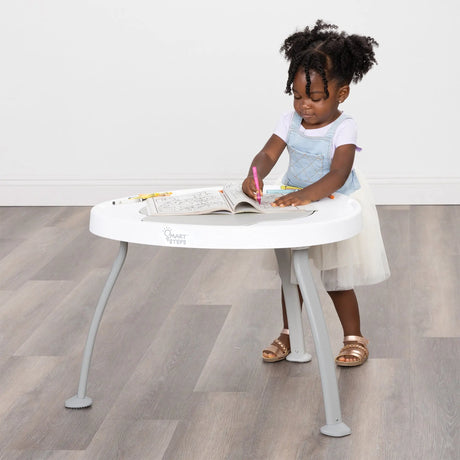 A child coloring using the Smart Steps Hop N' Discover 3-in-1 Activity Center as a table