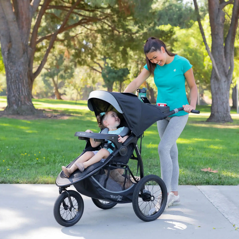 Mother checking on her child through the canopy peek-a-boo window with the Baby Trend Expedition Race Tec Plus Jogger Stroller at the park