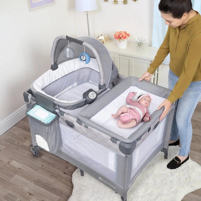 A mother looking after her child laying in the Lullaby Nursery Suite EZ-Fold Playard with Portable Rocking Lounger