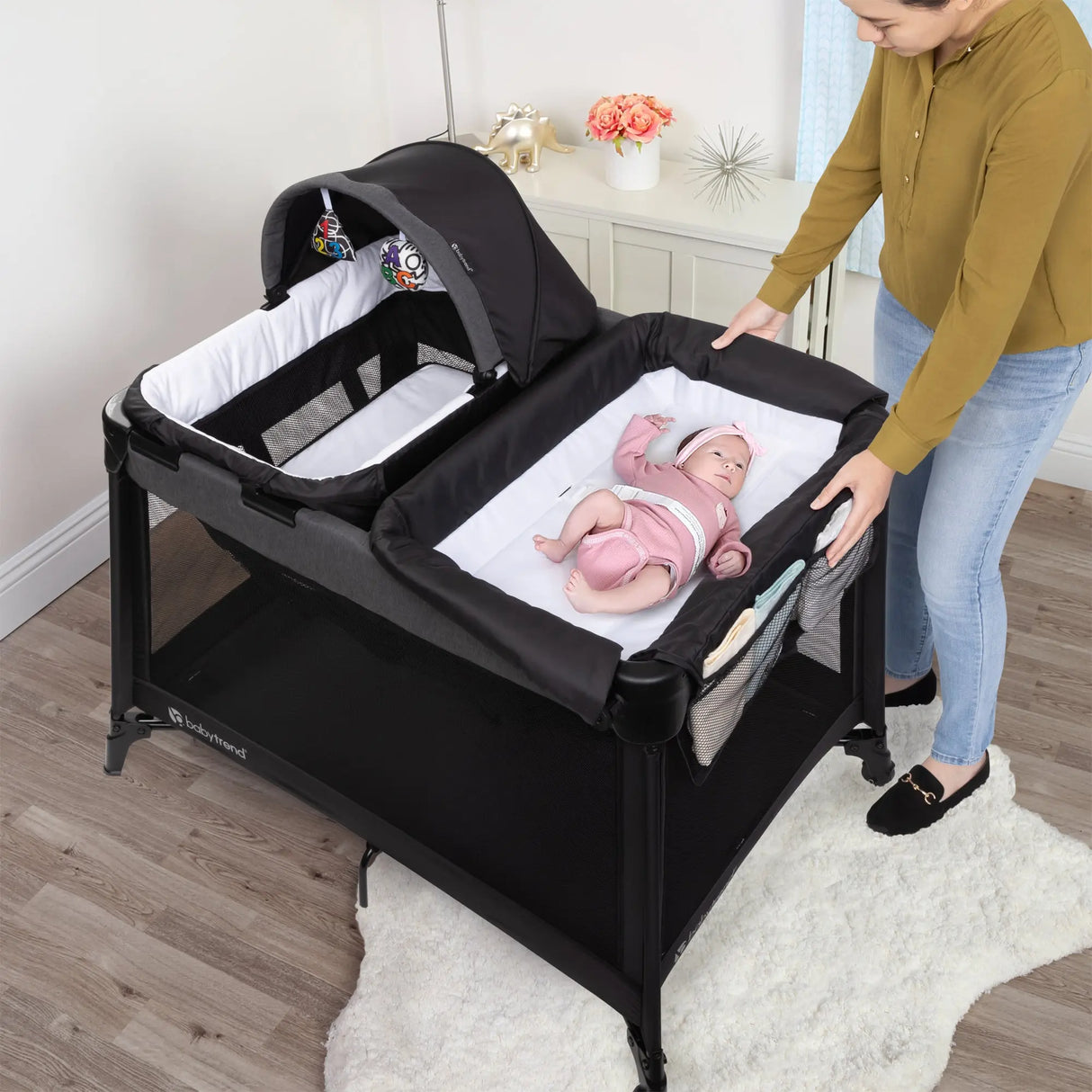 A child is laying on the changing table of the Baby Trend Willow Nursery Center Playard while the mom looking after the baby 