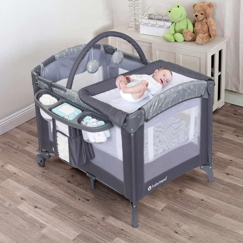 A child laying on the changing table of the Baby Trend EZ Rest Deluxe Nursery Center Playard