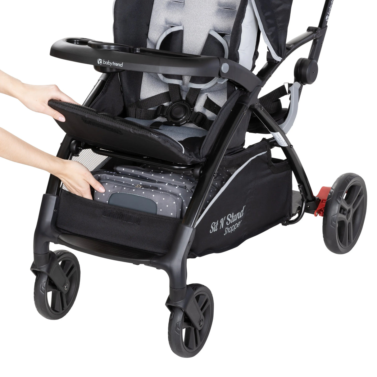 A person is accessing the storage basket from the front of the Baby Trend Sit N Stand 5-in-1 Shopper Stroller