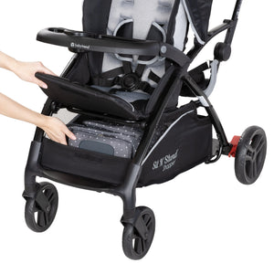 A person is accessing the storage basket from the front of the Baby Trend Sit N Stand 5-in-1 Shopper Stroller