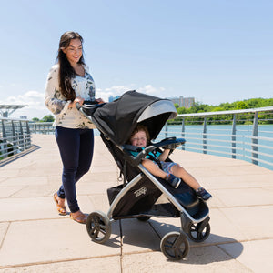 A mom pushing her child sitting in the Baby Trend Tango Stroller at a park