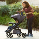 Load image into gallery viewer, Mom is looking through the canopy peek-a-boo window to check on her child seating in the Baby Trend Passport Carriage Stroller