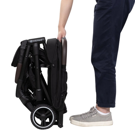 Side view of a person just finishing folding the Baby Trend Zenda Compact All-Terrain Stroller 