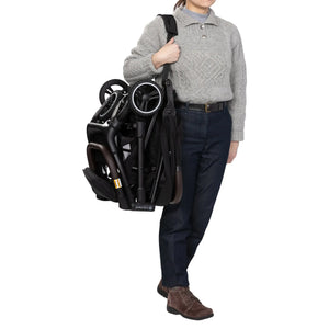A person is carrying the Baby Trend Zenda Compact All-Terrain Stroller folded with the shoulder strap