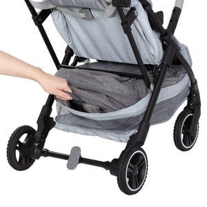 A person is pulling out a bag from the storage basket of the Baby Trend Zenda Compact All-Terrain Stroller