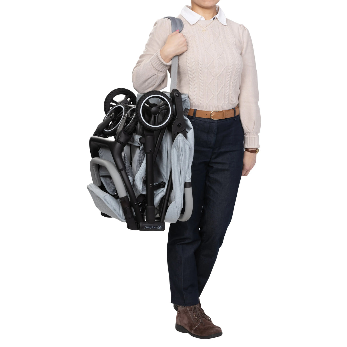 A person is carrying the folded Baby Trend Zenda Compact All-Terrain Stroller on their shoulder using the strap