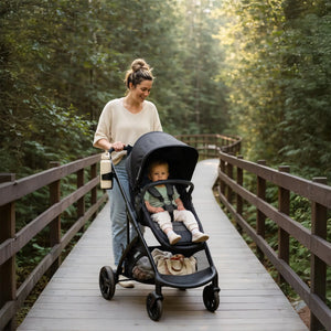 A mom is pushing her child sitting in a Baby Trend Passport Switch 6-in-1 Modular Stroller while going through the woods on a wooden bridge