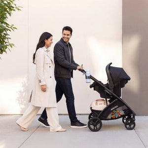 Parents walking on the sidewalk while pushing their child in the Baby Trend Passport Switch 6-in-1 Modular Stroller with the car seat attached 