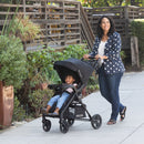 Load image into gallery viewer, A mother is strolling with her child outside with the Baby Trend Passport Carriage DLX Stroller Travel System
