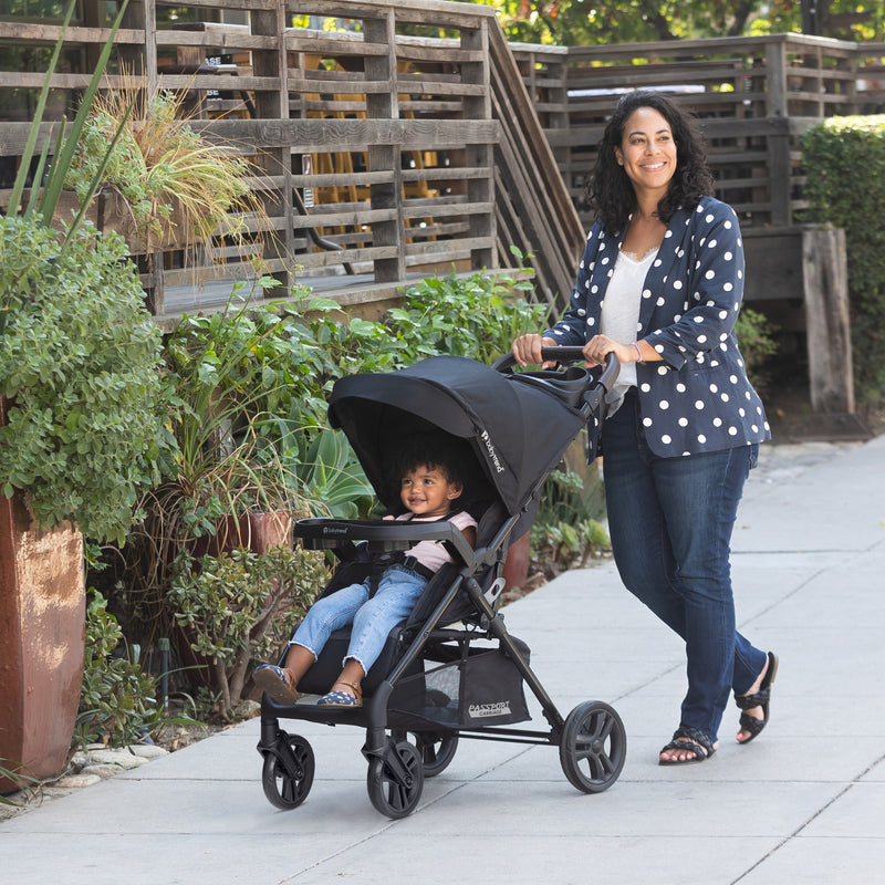 A mother is strolling with her child outside with the Baby Trend Passport Carriage DLX Stroller Travel System