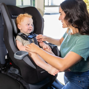 A mom is placing the harness on her child sitting the Baby Trend Trooper Convertible Car Seat