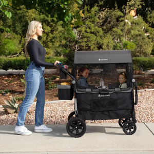 A mom is pushing her two children sitting in the Baby Trend Quest 3-in-1 Stroller Wagon