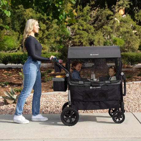 A mom is pushing her two children sitting in the Baby Trend Quest 3-in-1 Stroller Wagon