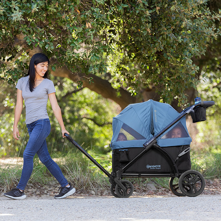 A mom is pulling her two children sitting in the Baby Trend Navigator stroller wagon