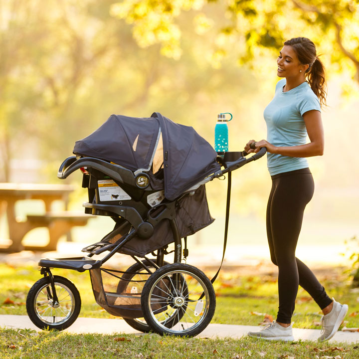 Baby Trend jogger stroller travel system of mother strolling with her infant in the car seat setting in the park