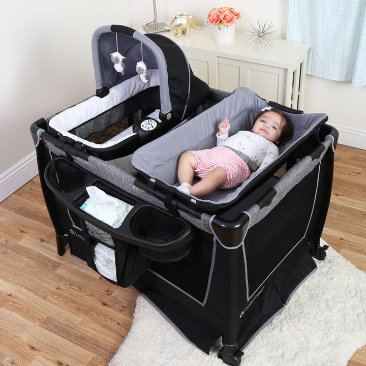 A child is on the safe surround changing table on a Baby Trend Nursery Center Playard with Rock-a-Bye Bassinet