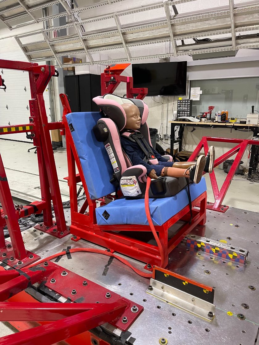 A crash-test dummy secured in a Baby Trend car seat mounted on the test sled