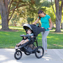 Load image into gallery viewer, Mother checking on her child through the canopy peek-a-boo window with the Baby Trend Expedition Race Tec Plus Jogger Stroller at the park