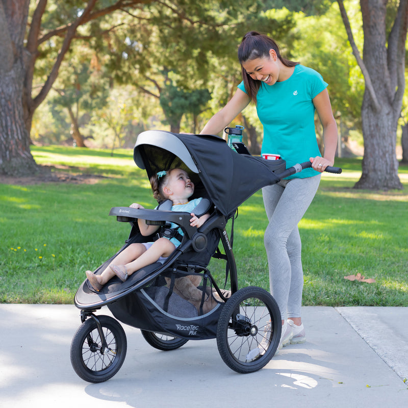 Mom is checking on her child through the canopy of the Baby Trend Expedition Race Tec Plus Jogger Stroller