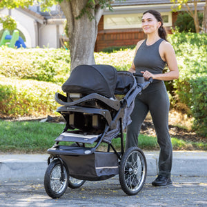 Mom is outdoor pushing the Baby Trend Expedition Jogger Stroller Travel System