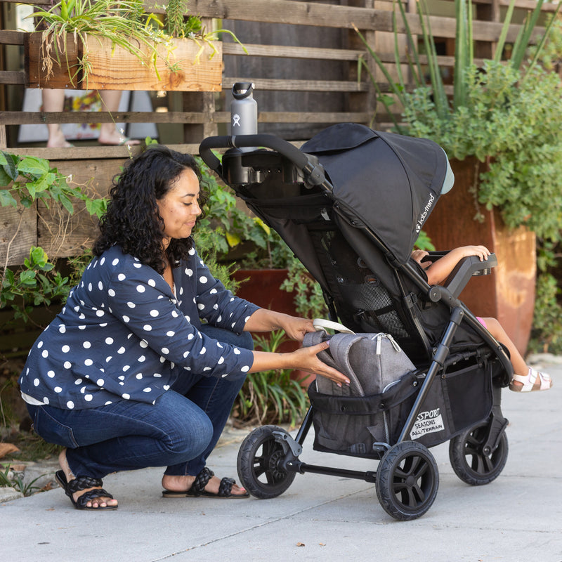 Adventuring in the outdoor with her child, the mom access the extra large storage basket from the Baby Trend Passport Seasons All-Terrain Stroller Travel System